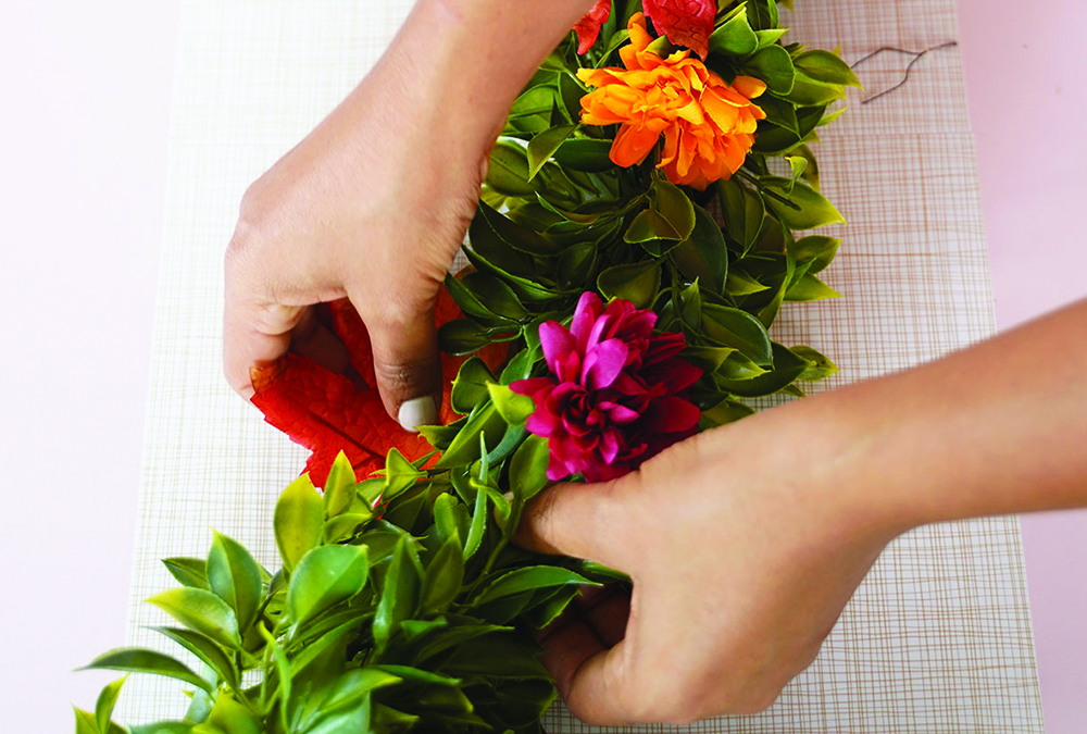 hands adding colorful flowers to garland